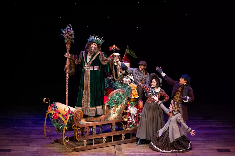 Image: A man in green rides a sleigh with people behind him.