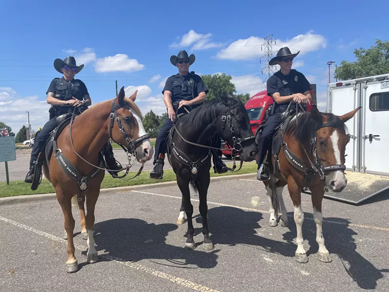 Image: Three horses (two brown and one black) stand with police officers on top of them.