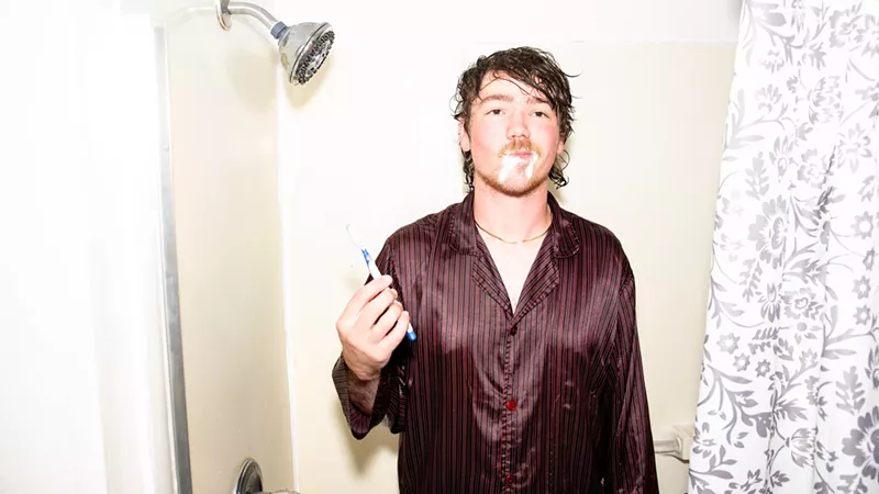 Image: man brushes teeth in the shower wearing a brown silk shirt