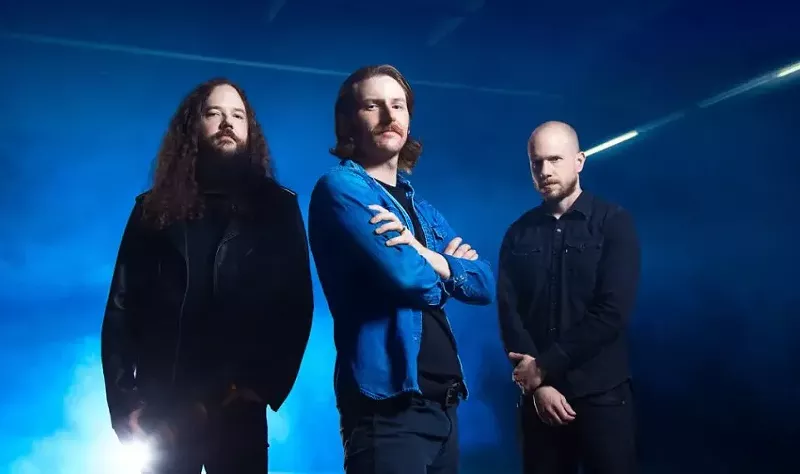 Image: three men pose in a blue room