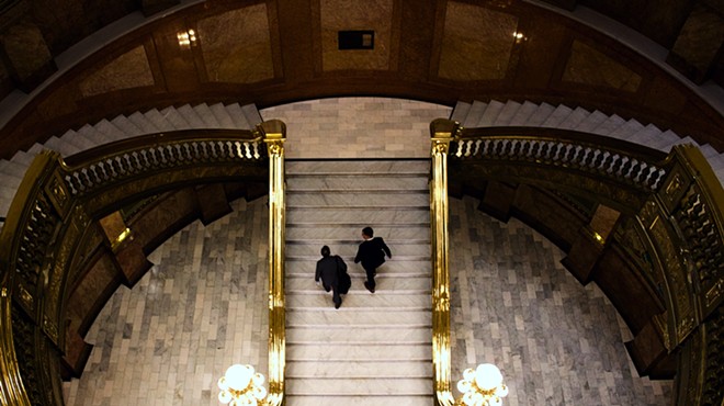 Two men in suits walk up the stairs of the Colorado Capitol building.