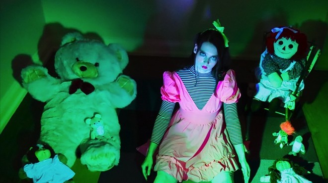 woman dressed as a doll in green lighting surrounded by teddy bears.
