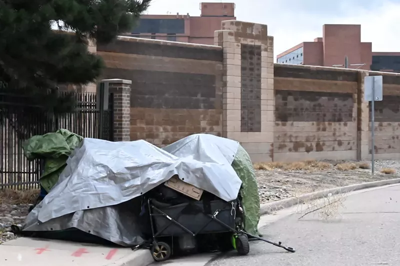 Image: A tent with belongings sits on a residential road in Aurora that runs on the other side of a wall along Interstate 225.