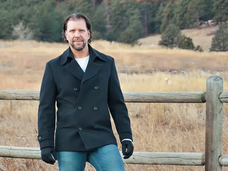 Image: man leans on a fence outdoors wearing jeans and a coat