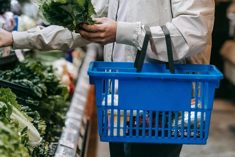 Image: A man carries a blue hand-held grocery basket while shopping.