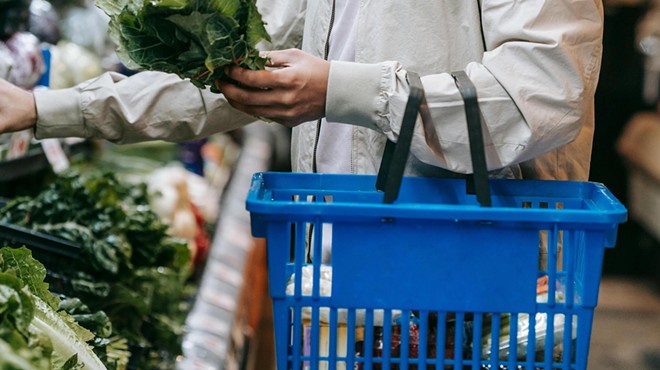 A man carries a blue hand-held grocery basket while shopping.