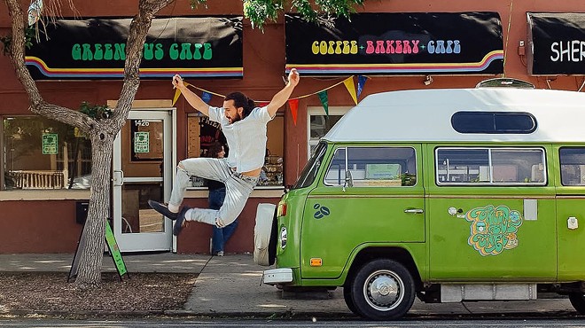 a man jumping in the air next to a vintage green bus