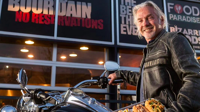 man standing next to a motorcycle holding a tray of hot dogs