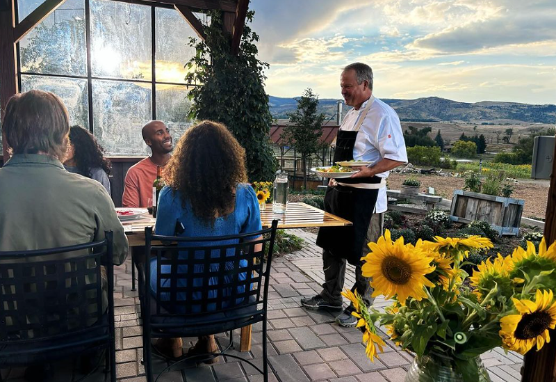 Image: man in a apron serving food to guests at a table