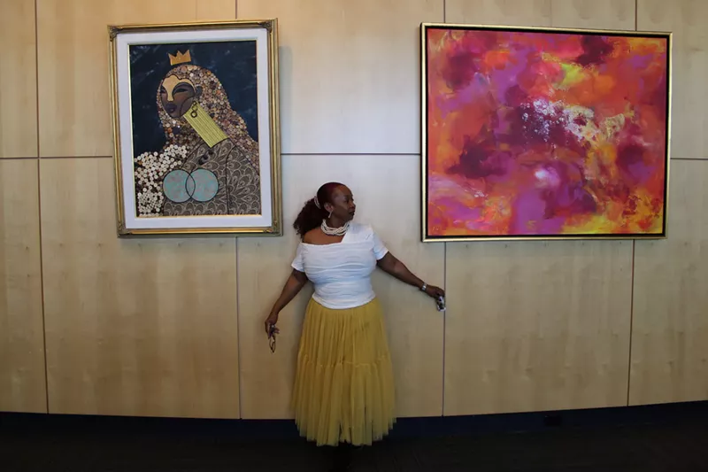 Image: Black woman stands in front of two paintings.