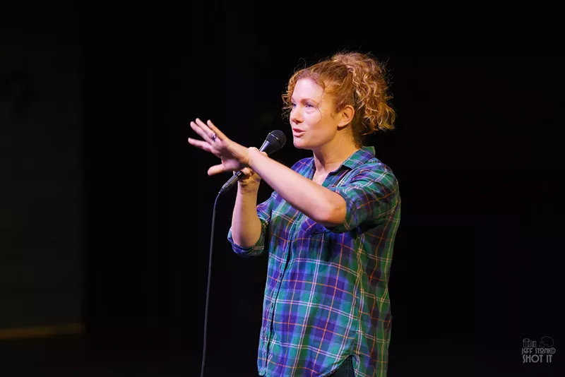 Image: A comedian speaks into a microphone onstage.