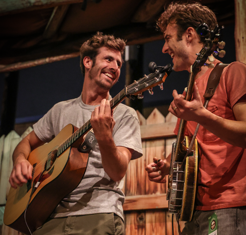 Image: man playing guitar smiles at man playing banjo