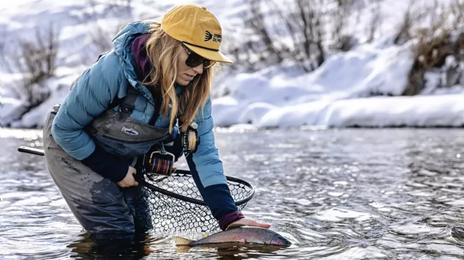 A female fly fishing guide releasing a trout into a river