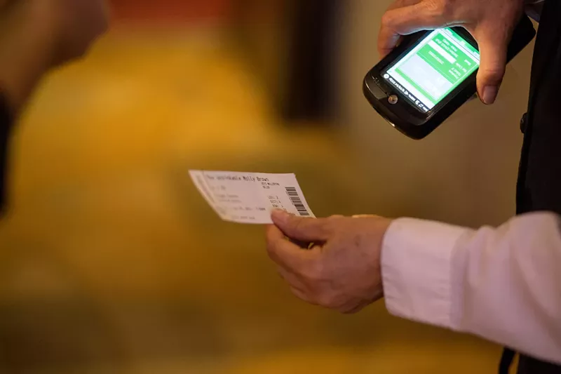 Image: A ticket is held in one hand and scanned with the other by an attendee.