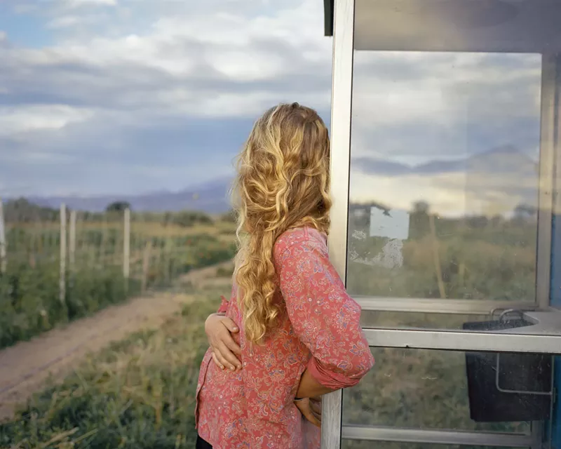 Image: blonde woman leaning on a window looking out at the countryside
