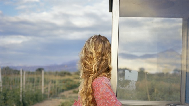 blonde woman leaning on a window looking out at the countryside