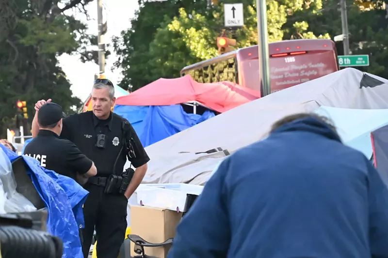 Image: Denver Police officers talk at the corner of 8th Avenue and Logan Street.