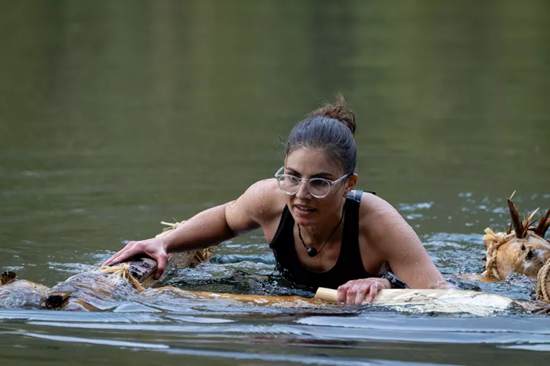 Image: Rose Hyak submerged in water and floating on a primitive raft during a survival challenge