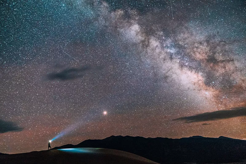 Image: A person wearing a headlamp while hiking beneath the Milky Way at Great Sand Dunes National Park