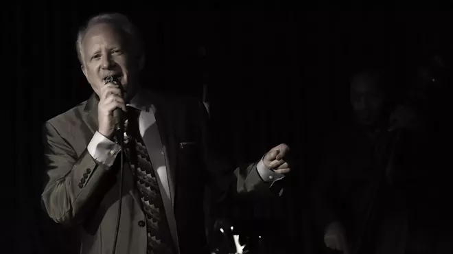 A man in a suit sings with a microphone on stage.