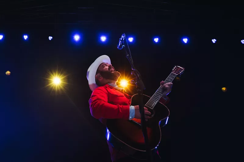 Image: man in white hat and red shirt playing the guitar