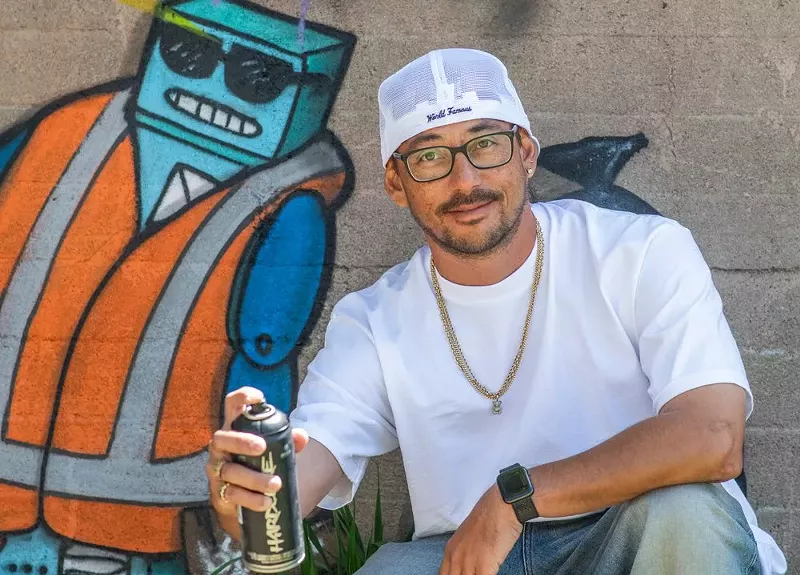 Image: man in hat with spraypaint against mural