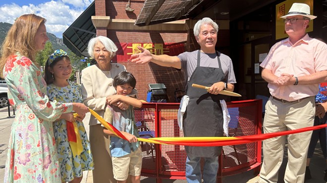 man in an apron standing with family and cutting a ribbon