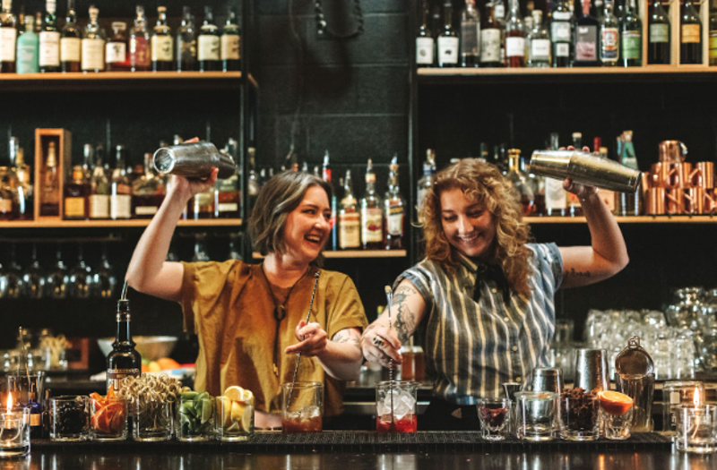 Image: two women shaking drinks behind a bar