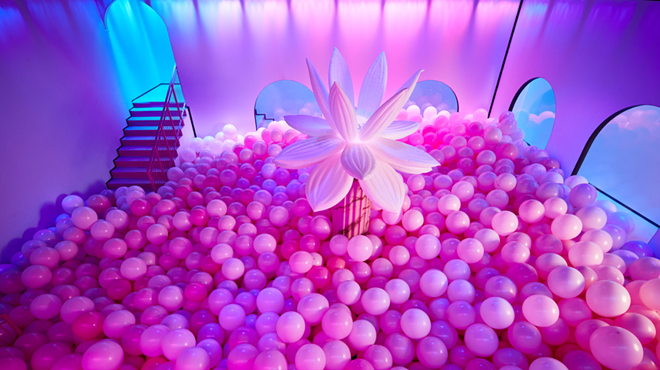 pink balloons on the floor of a room with an inflatable flower in the center