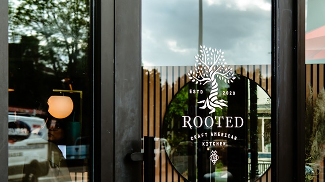 a black sign that says "rooted" behind a glass door