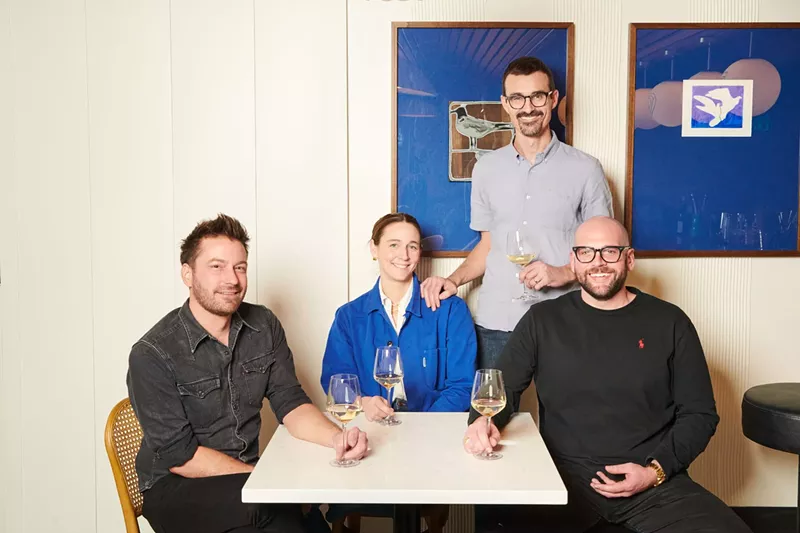 Image: three people sitting at a white table and one standing