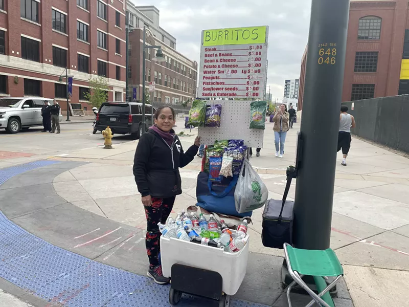 Image: A woman stands on the corner with a cart containing ballpark snacks.