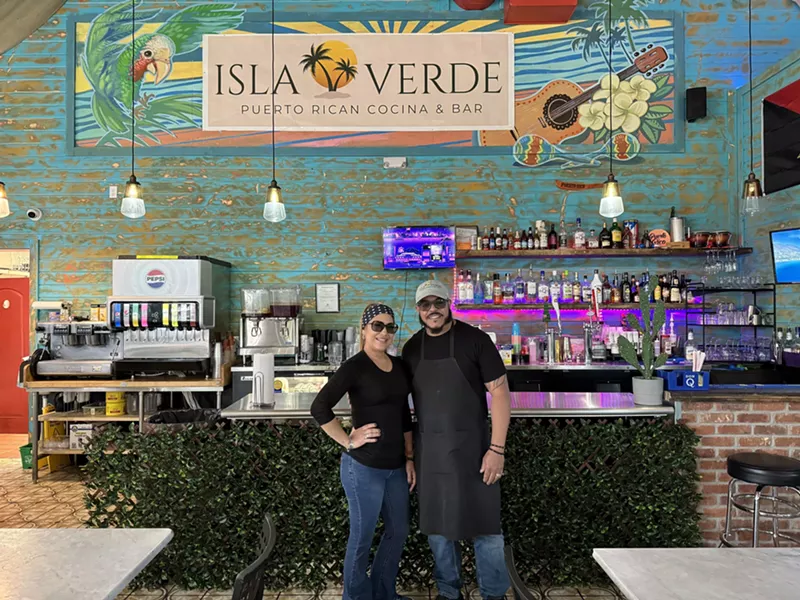 Image: a woman and man posting in front of an "isla verde" sign