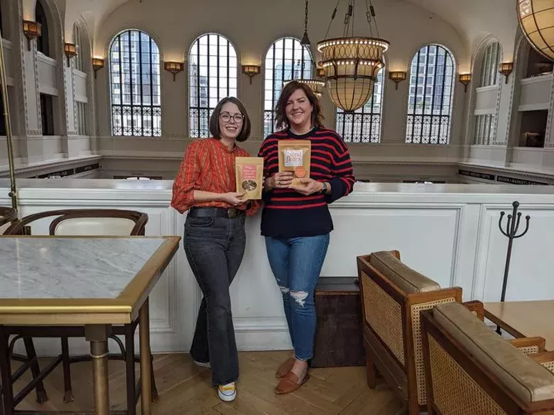 Image: two woman standing, each holding a food package