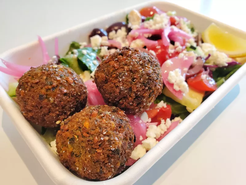 Image: three falafel on top of a salad with onions, feta, lettuce and tomatoes