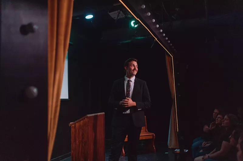 Image: moustached young man in a suit and tie on a stage