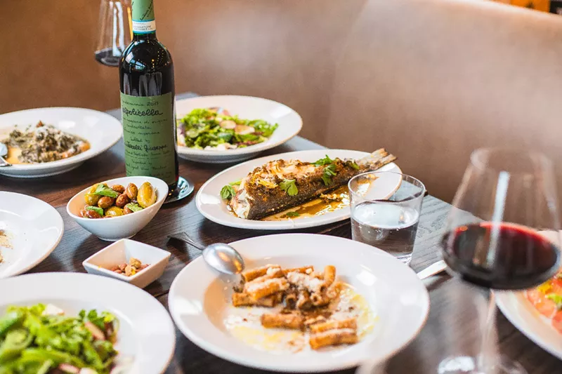 Image: various foods on white plates set on a table with a bottle of wine