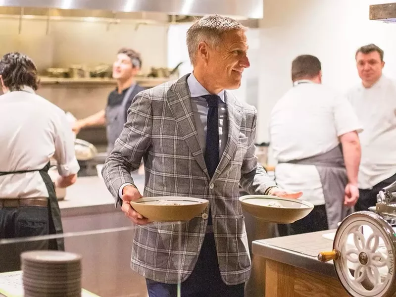Image: a man in a suit holding plates in a kitchen