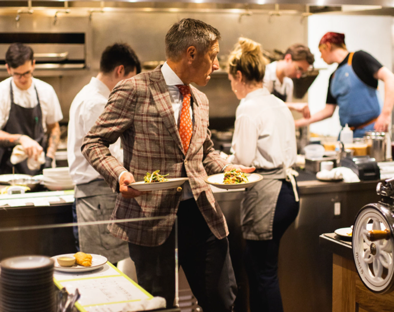 Image: a man in a suit holding plates in a kitchen