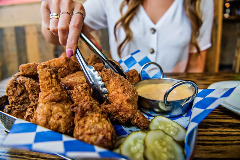Image: A woman using tongs to pick up fried chicken