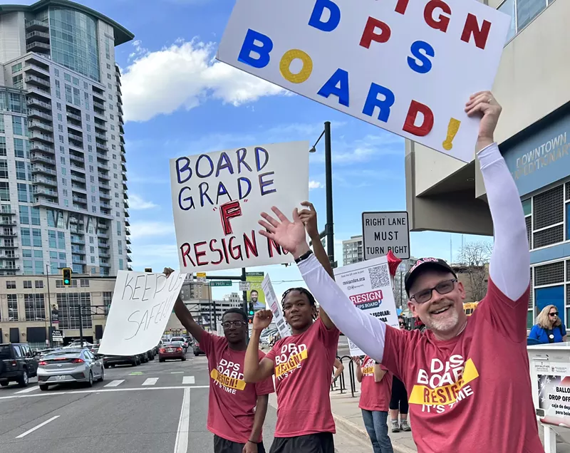 Image: Two students and one parent stand on the side of the road wearing "Resign DPS" shirts and holding signs calling for board members to step down.