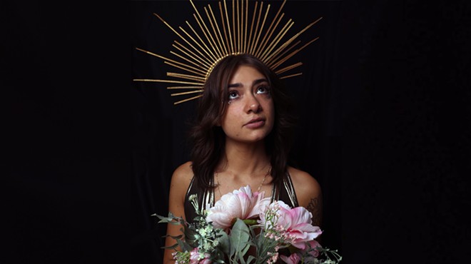 brunette woman wearing gold crown and holding pink flowers.