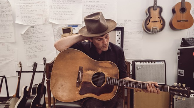 man in fedora poses with his acoustic guitar