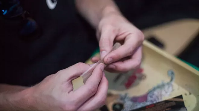 Hands roll a marijuana joint over a RAW tray