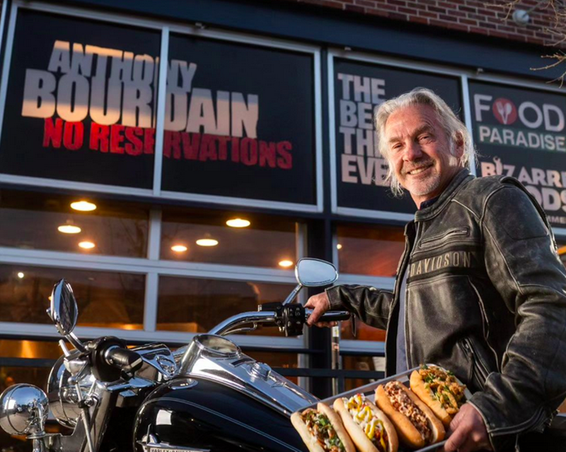 Image: man standing next to a motorcycle holding a tray of hot dogs