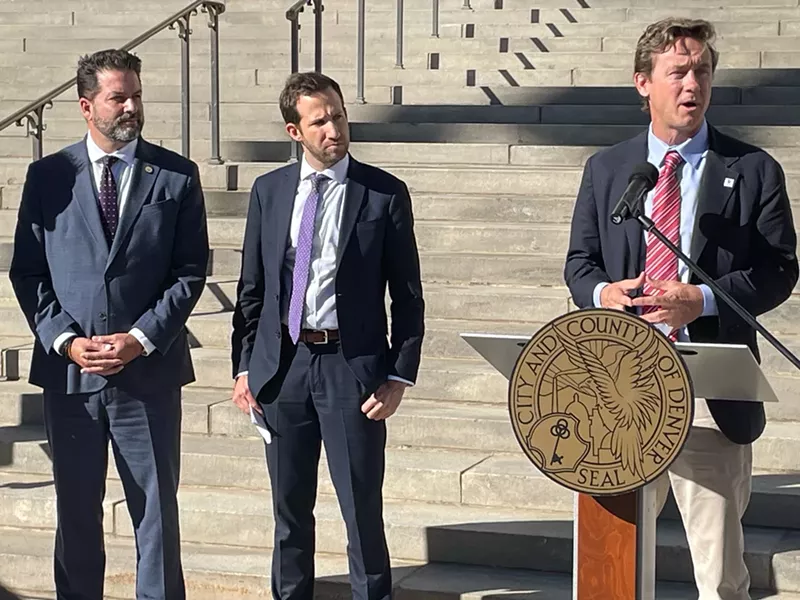 Image: Mayor Mike Johnston speaks alongside a pair of high-ranking federal officials.