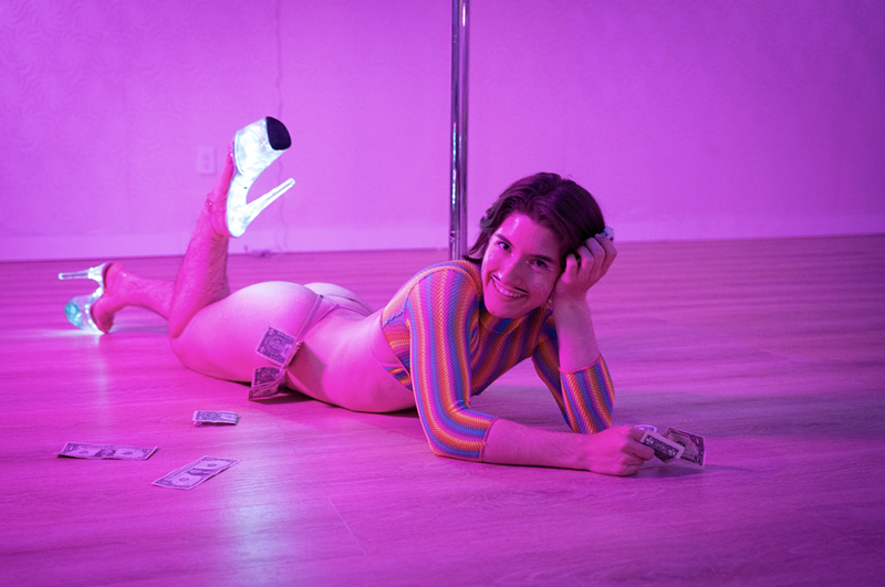 Image: A pole dancer poses by a pole.