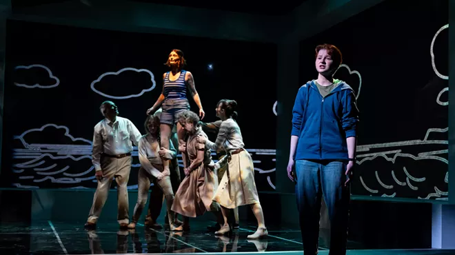 A boy stands while a woman is raised by a crowd behind him.