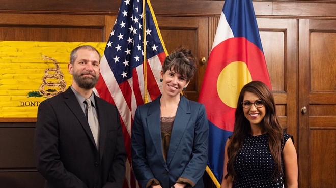 Three people smiling and posing for a picture together in front of the US flag and state flag of Colorado.