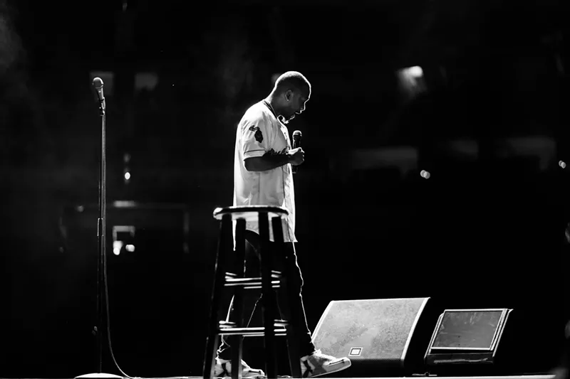 Image: man in white t-shirt standing on stage with microphone
